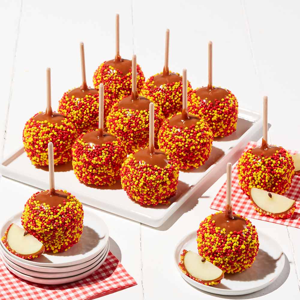 Caramel apples with colorful sprinkles on sticks, served on a white tray and plates.