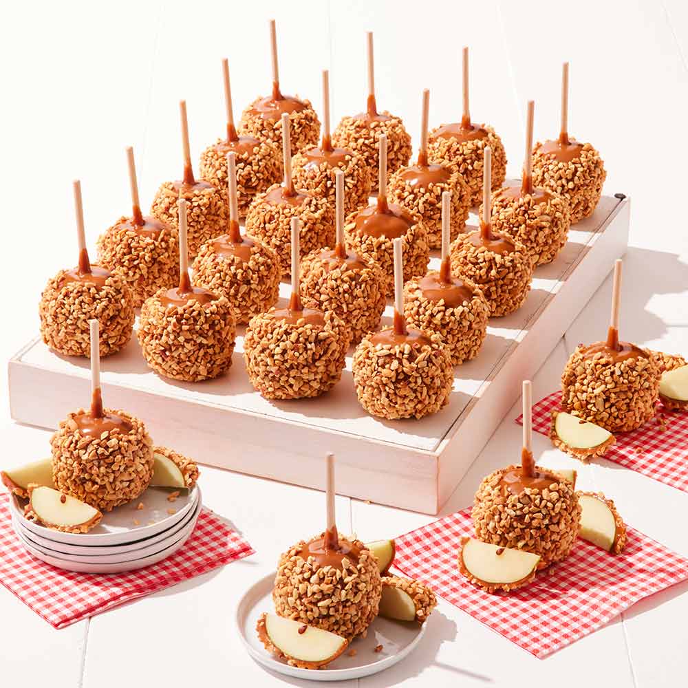 Caramel apples with nuts on sticks displayed on a white stand with red checkered napkins.