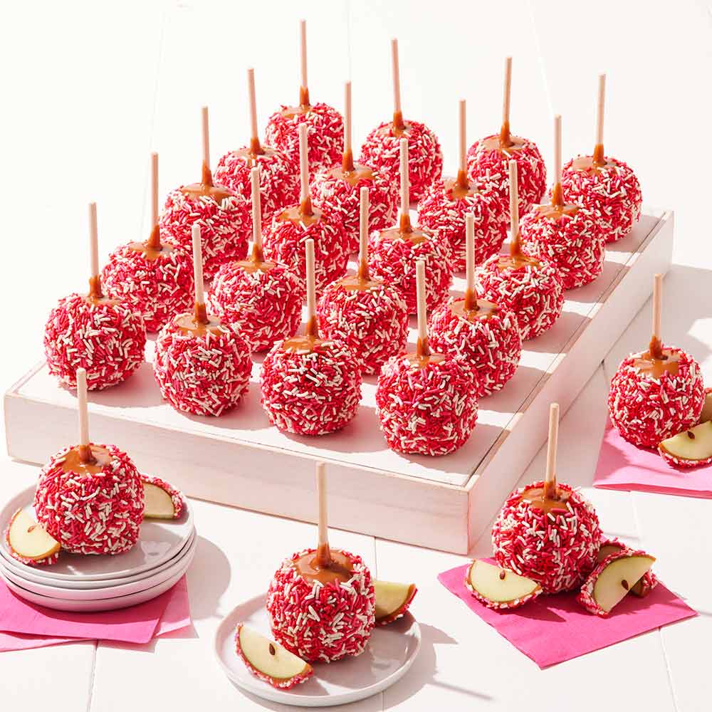 Caramel apples with red coating and sprinkles on a white stand with pink napkins.
