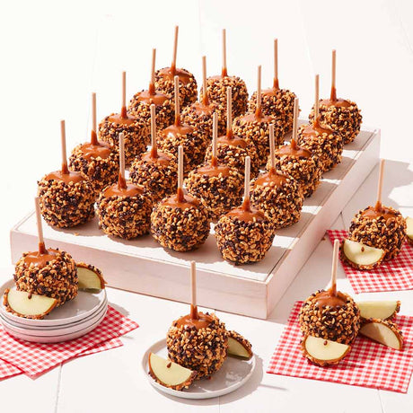 Caramel apples on sticks displayed on a white tray with red checkered napkins.
