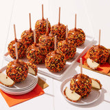 Caramel apples with colorful toppings on a white surface with orange napkins.