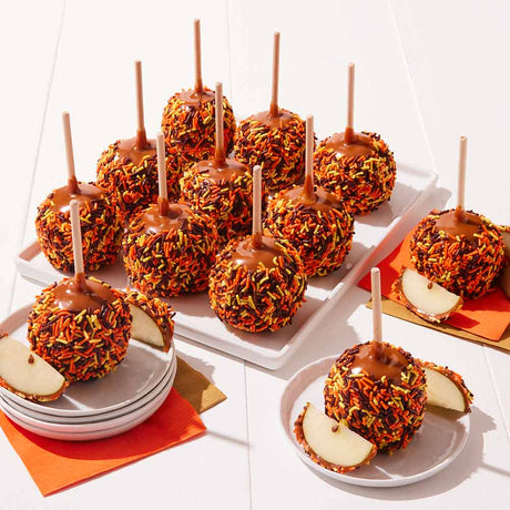 Caramel apples with colorful toppings on a white surface with orange napkins.