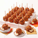 Assorted caramel apples on sticks displayed on a white tray with orange napkins.