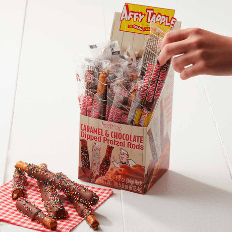 Box of Affy Tapple caramel and chocolate-dipped pretzel rods with a hand reaching for one.