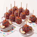 Caramel apples with colorful sprinkles on sticks on a white surface.