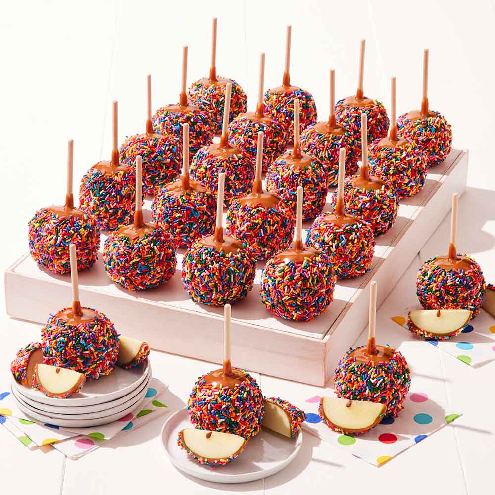 Colorful caramel apples with sprinkles on sticks displayed on a white surface.