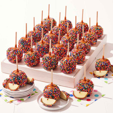 Colorful caramel apples with sprinkles on sticks displayed on a white surface.