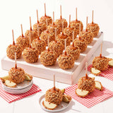 Caramel apples with nuts on sticks displayed on a white stand with red checkered napkins.
