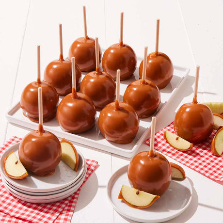 Caramel apples on sticks displayed on a white tray with red checkered tablecloth.