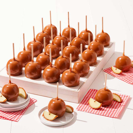Caramel apples on sticks displayed on a white surface with red checkered napkins.
