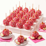 Caramel apples with red coating and sprinkles on a white stand with pink napkins.